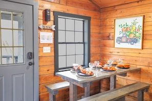 A wooden cabin interior with a dining table set for four, a window with a view, and a wall-mounted light fixture. - Starlight Summit Big Buck Hunter Arcade Hot Tub (Sevierville)