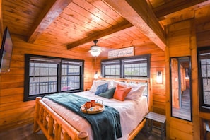 Une chambre dans une cabane en bois, avec un lit, des fenêtres, une enseigne et un plateau avec des tasses.