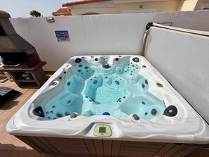 Un bain à remous doté d’un panneau de commande, entouré d’une terrasse carrelée.