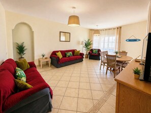 Una sala de estar con un sofá rojo, una mesa de comedor con sillas, una mesita auxiliar, una lámpara y un letrero que dice 'WELCOME'.