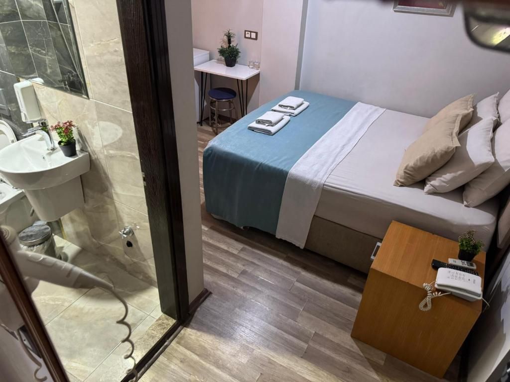 Een hotelkamer met een bed, nachtkastje, bureau, stoel en een badkamer met een wastafel en spiegel.