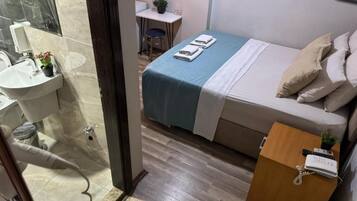 Een hotelkamer met een bed, nachtkastje, bureau, stoel en een badkamer met een wastafel en spiegel.