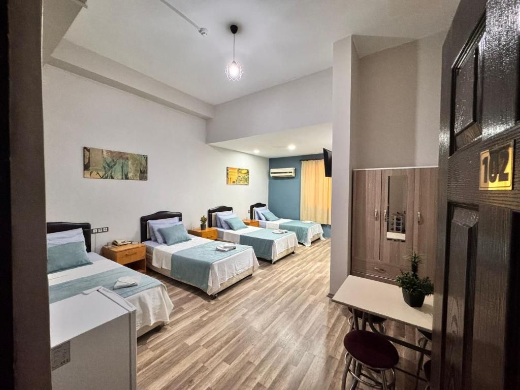 A hotel room with four single beds, a small table, a chair, a TV, and a wooden floor.