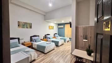 A hotel room with four single beds, a small table, a chair, a TV, and a wooden floor.