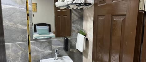 A bathroom with a marble wall, a sink, a towel rack, and a wooden door.