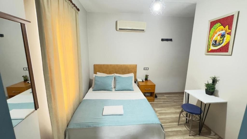 Habitación de hotel con cama, mesita de noche, silla, escritorio y un cuadro en la pared.