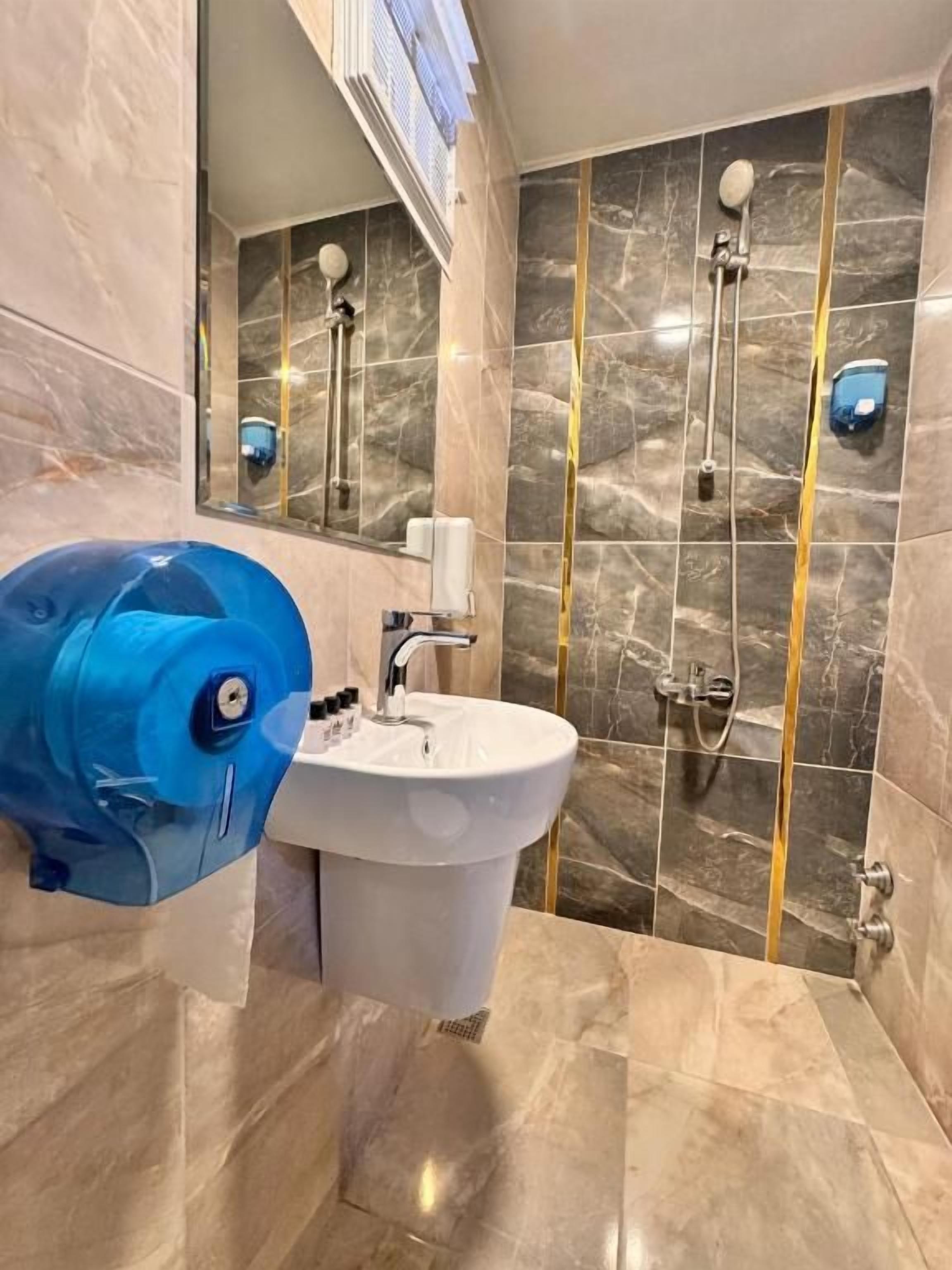 A bathroom with a marble floor, a sink, a blue water heater, and a shower with a gold accent wall.