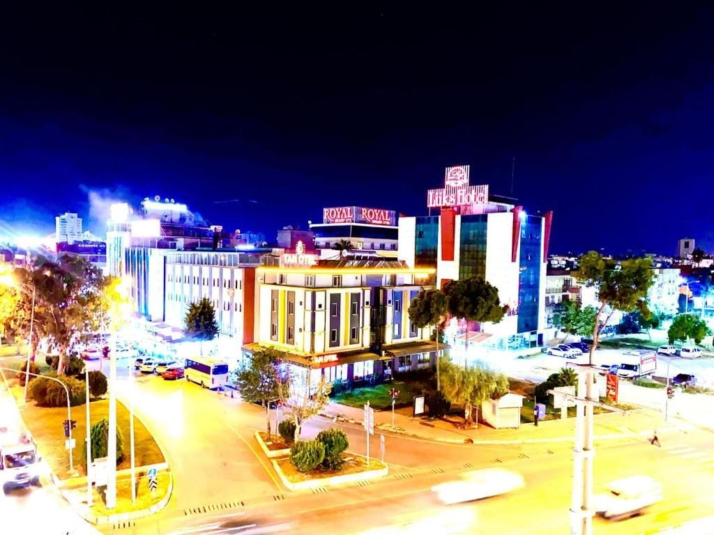 A brightly lit hotel with a prominent sign, a parking lot, and a street view at night.