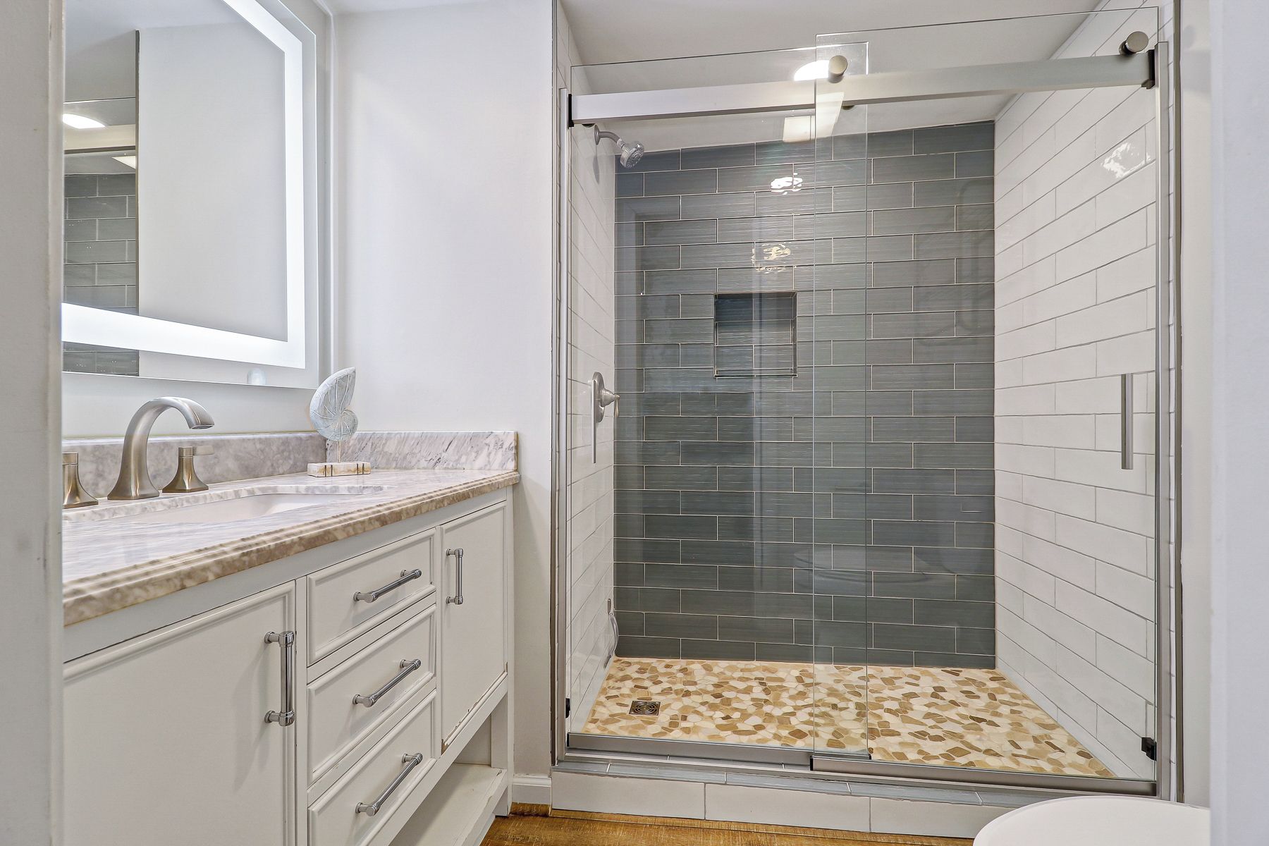 Une salle de bain moderne avec une douche à parois de verre, un comptoir en marbre et un grand miroir.