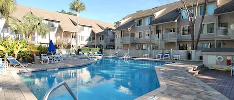 Une piscine dotée de chaises longues et d’un espace aménagé au bord de l’eau, le tout entouré d’immeubles à plusieurs étages dotés de balcons.