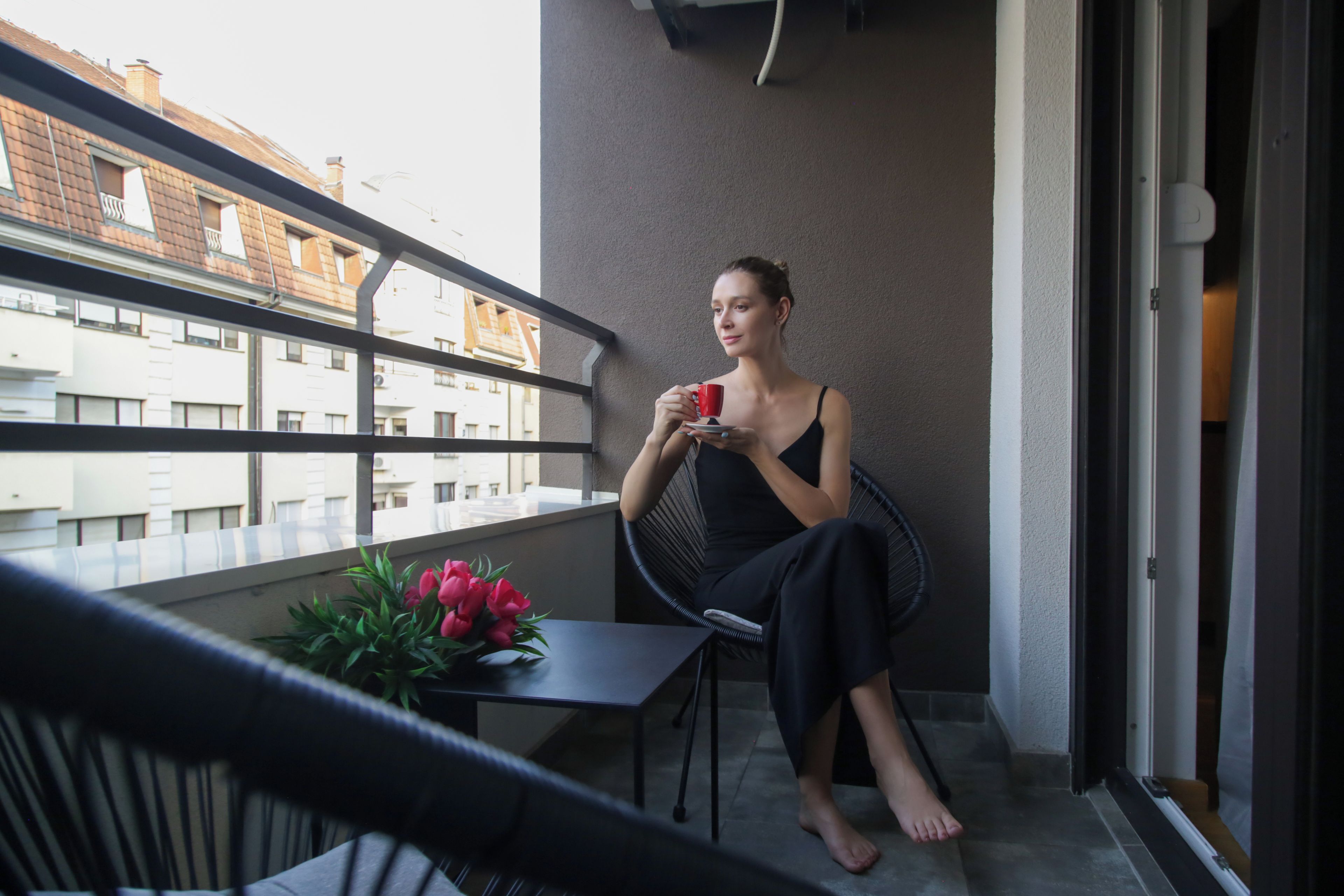 Une personne assise sur une chaise de balcon, avec une table et un bouquet de fleurs à proximité.