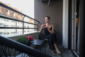 A person sitting on a balcony chair with a table and a bouquet of flowers. - Supernova DeLuxe Residence 2bdr Apartment in Novi Sad with AC for relaxing stays (Novi Sad)