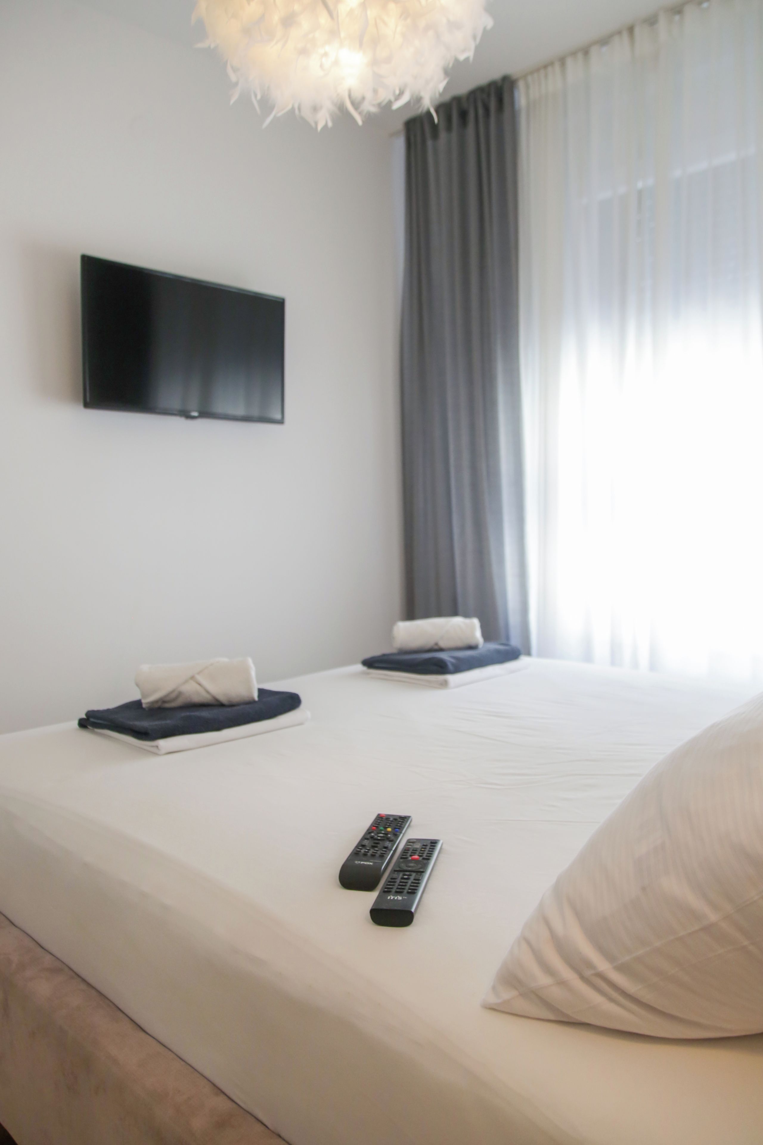 Une chambre d’hôtel avec un lit, deux oreillers, un téléviseur à écran plat fixé au mur et deux télécommandes posées sur le lit.