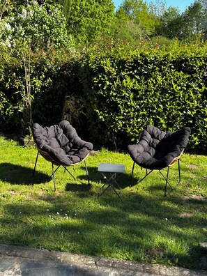Two black cushioned chairs with a small table in a grassy outdoor area, surrounded by dense greenery and trees. - New Listing (Saint-Cirgues-de-Malbert)