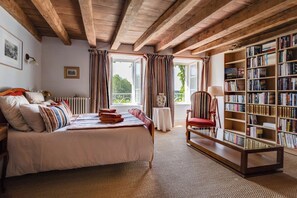 Un dormitorio con una cama grande, una estantería, una silla y una ventana con cortinas.