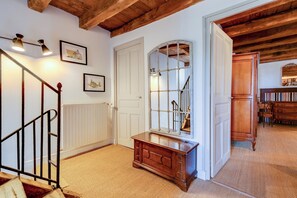 Een gang met een houten trap, een radiator en een houten bankje.