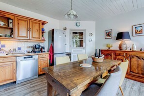 Een keuken met houten kastjes, een RVS vaatwasser, een koelkast en een eettafel met stoelen.