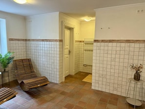 Ein Badezimmer mit gefliestem Boden, einer Bank, einem Heizkörper und einem kleinen Tisch mit einer Vase.