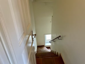 Eine Treppe mit Geländer, eine Tür links und ein Fenster oben.