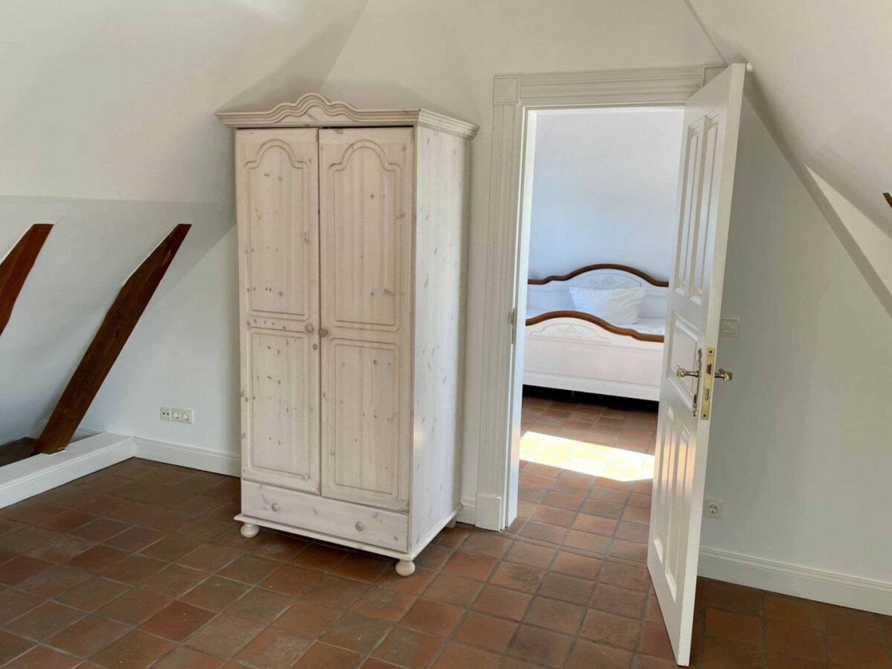 A bedroom with a white wardrobe, a bed with a wooden headboard, and a sloped ceiling.