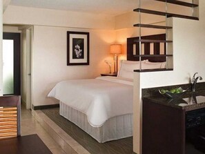 Ein Hotelzimmer mit Bett, Nachttisch, Lampe, einem gerahmten Bild an der Wand und einem Badezimmer mit Waschbecken und Spiegel.