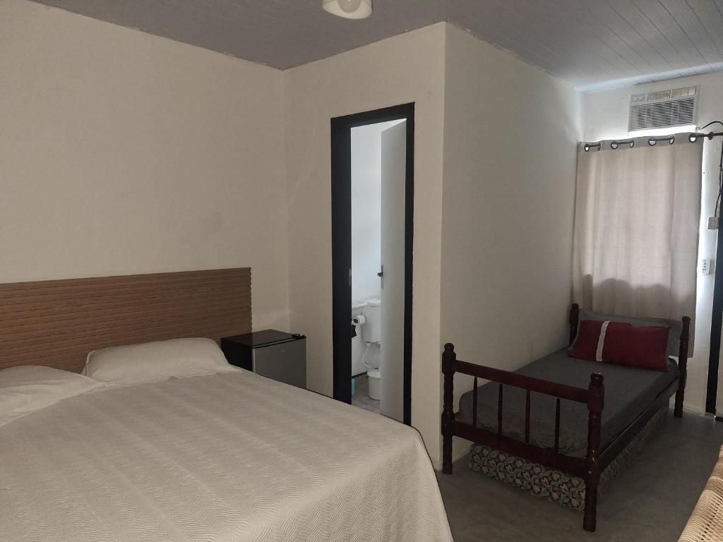 Quarto com duas camas, cabeceira de madeira, mesa de cabeceira pequena e janela com cortinas.