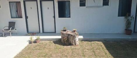 A building with two doors, numbered 9 and 8, a small outdoor seating area with a bench, and a tree stump.