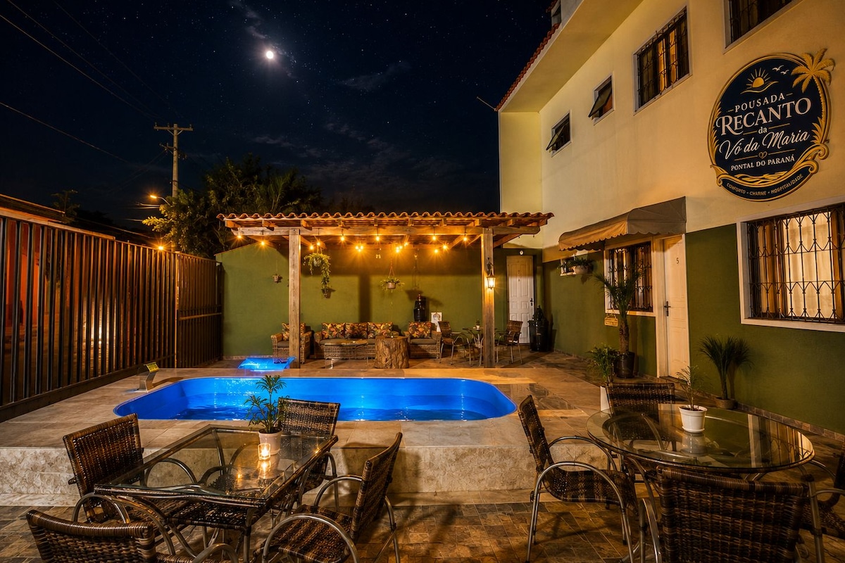 Un patio exterior nocturno con piscina, mobiliario de mimbre y una zona de estar cubierta.