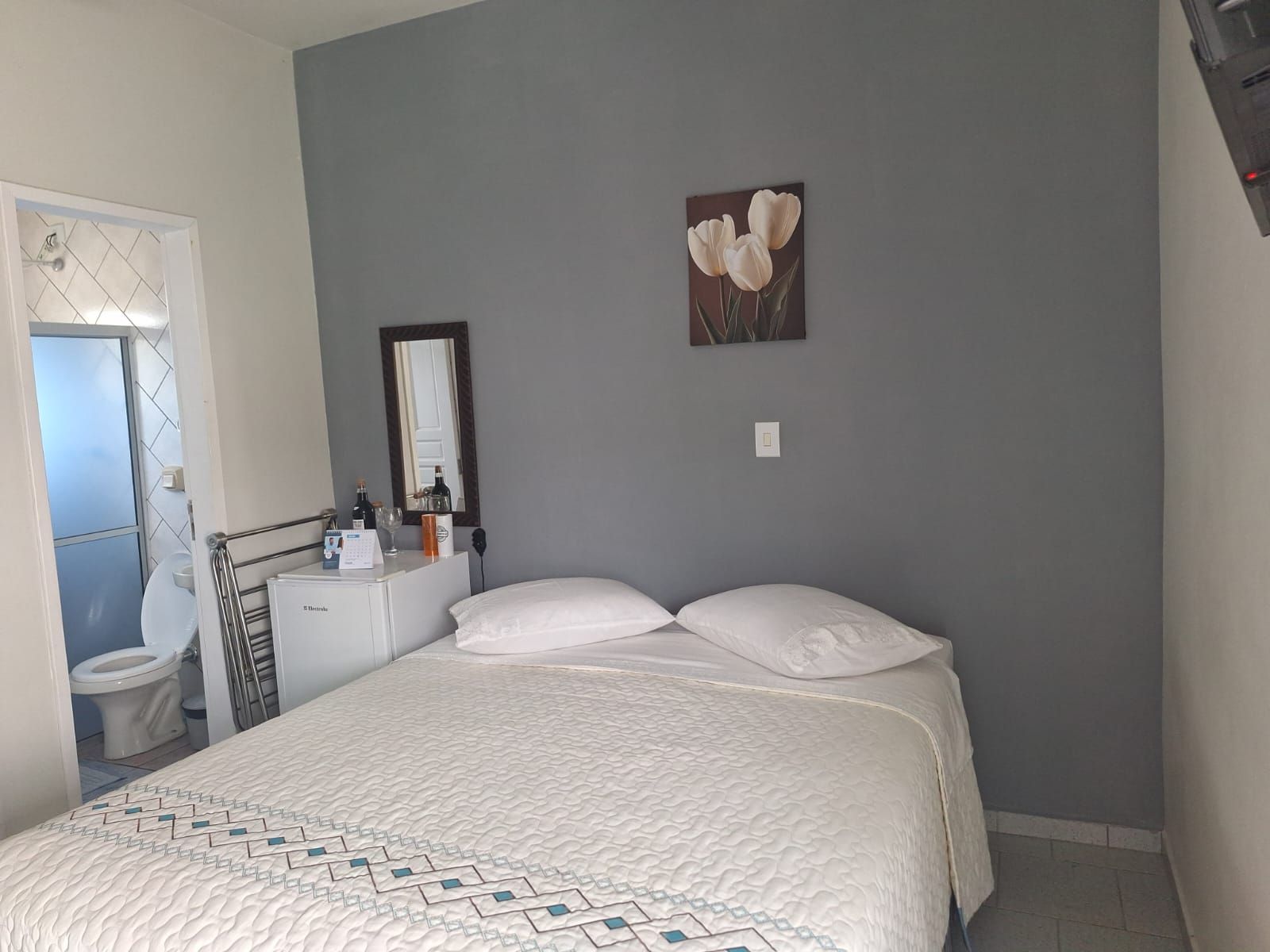 A bedroom with a bed, a bedside table, a mirror, and a wall-mounted picture.