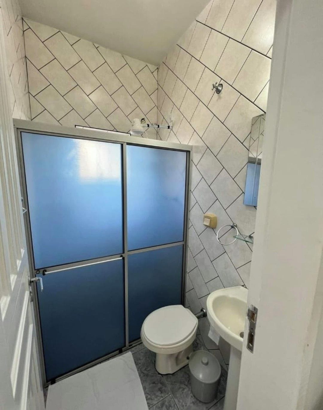 A bathroom with a toilet, sink, and a shower enclosure with a blue door.