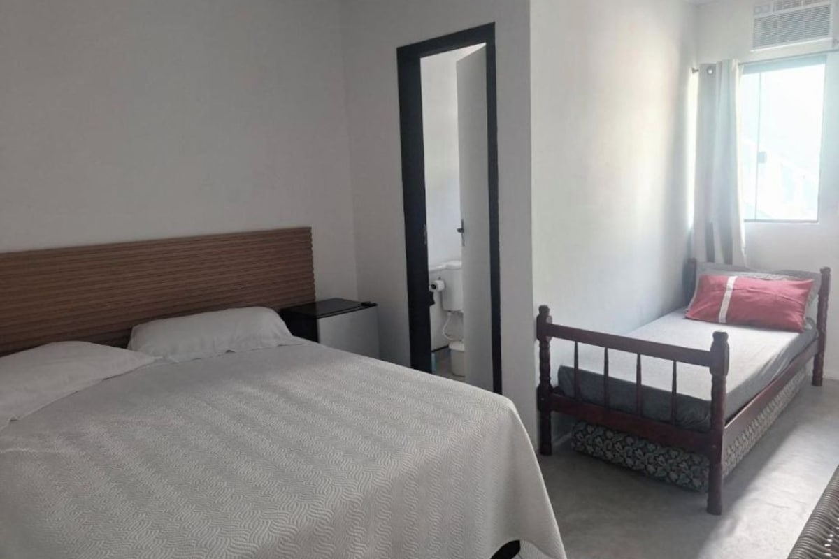 Un dormitorio con una cama grande, una cama más pequeña, una mesita de noche, un espejo y una ventana con cortinas.