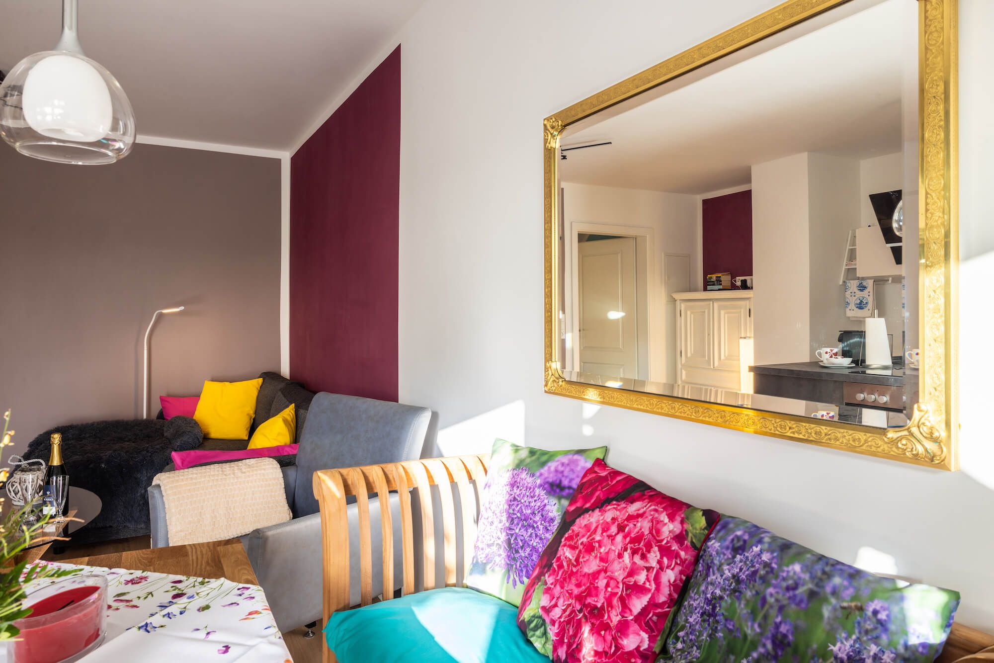 Un salon moderne avec un grand miroir, un canapé agrémenté de coussins colorés, une table à manger avec une bougie et une lampe.