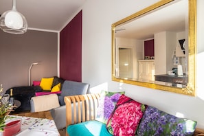 Een moderne woonkamer met een grote spiegel, een bank met kleurrijke kussens, een eettafel met een kaars en een lamp.