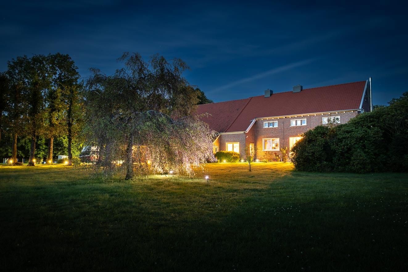 Een rijtjeshuis met een rood dak en bakstenen muren, omringd door een goed verlichte tuin in de schemering.