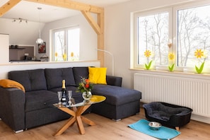 Ein modernes Wohnzimmer mit einem grauen Sofa, einem Glastisch und einem schwarzen Haustierbett.