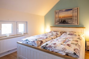 Een slaapkamer met een bed, twee ramen, een radiator en een schilderij aan de muur.