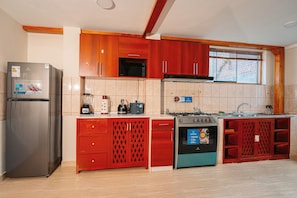 A kitchen with a stainless steel refrigerator, red cabinetry, a microwave, a kettle, a stove, and a dishwasher. - New Listing (Cusco)