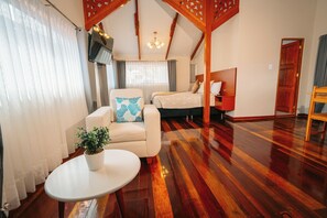 A spacious room with a wooden floor, a bed with a headboard, a seating area with a chair and a table, and a potted plant. - New Listing (Cusco)