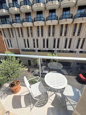 Ein Balkon mit Glastrennwand, zwei weiße Stühle, ein runder Tisch und ein Blumentopf.