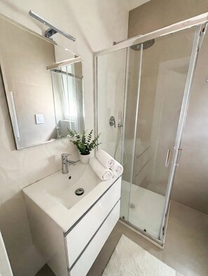 Um banheiro com toucador branco, espelho, planta e box de vidro.