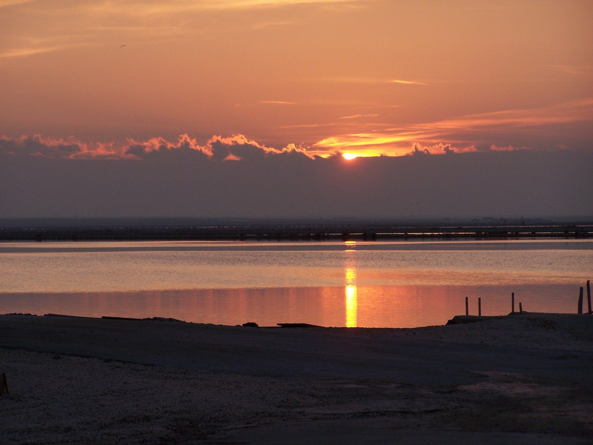 Un coucher de soleil sur une étendue d’eau calme, avec une côte lointaine à l’horizon.