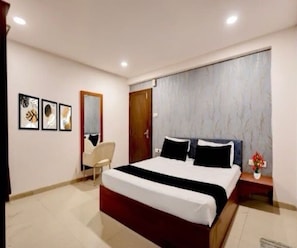 A bedroom with a large bed, a chair, a nightstand, and a wall with framed artwork. - Classic Hotel Expression (Indore)