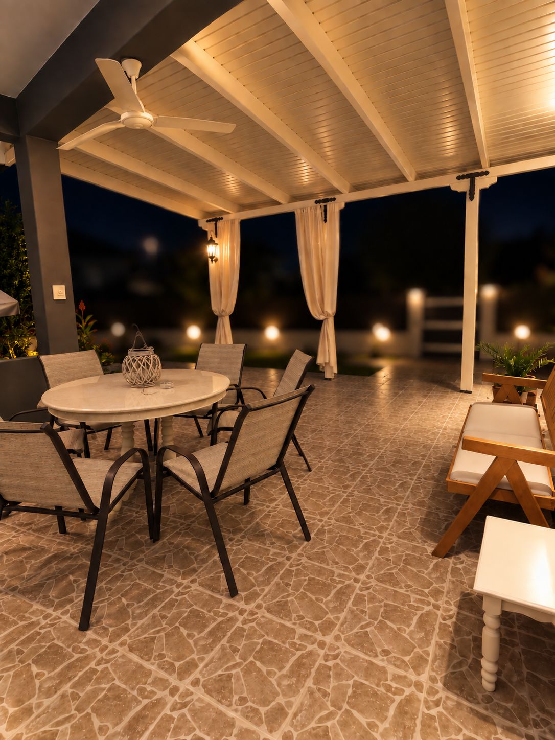 Une terrasse extérieure avec une table ronde et des chaises, un ventilateur de plafond et un éclairage d’ambiance.