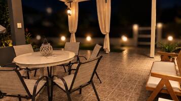 Une terrasse extérieure avec une table ronde et des chaises, un ventilateur de plafond et un éclairage d’ambiance.