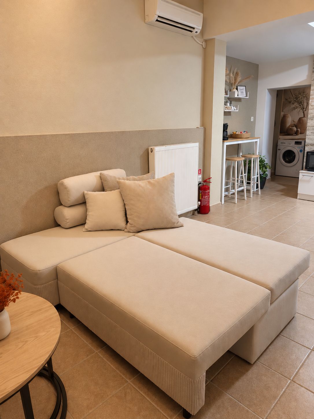 Ein modernes Schlafzimmer mit Schlafsofa, Heizkörper, Waschmaschine und einer kleinen Essecke.