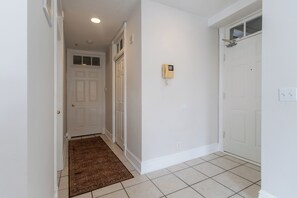 A hallway with white walls, a brown rug, and a door with a peephole. - Historic River District Downtown Escape (Fort Myers)