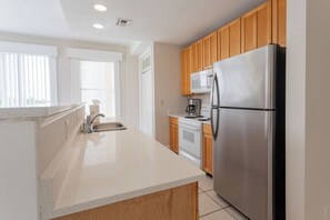 A modern kitchen with wooden cabinets, a stainless steel refrigerator, a microwave, and a coffee maker. - Historic River District Downtown Escape (Fort Myers)