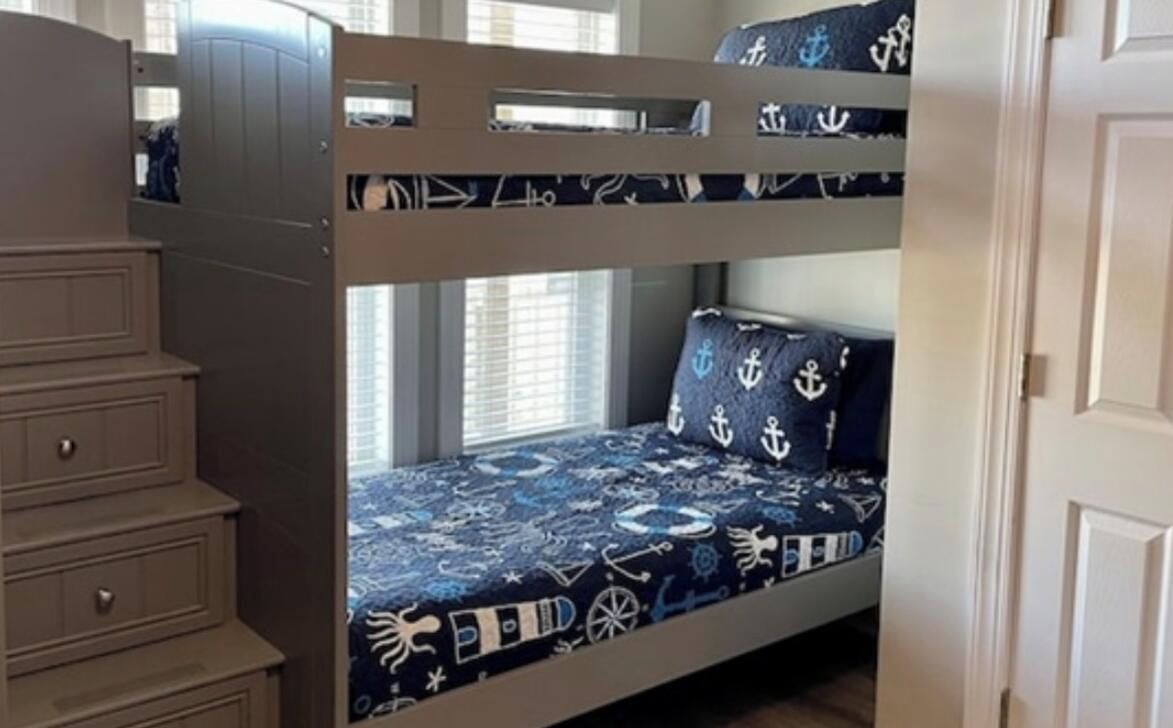 A bunk bed with a nautical theme, a dresser, and a window with blinds.