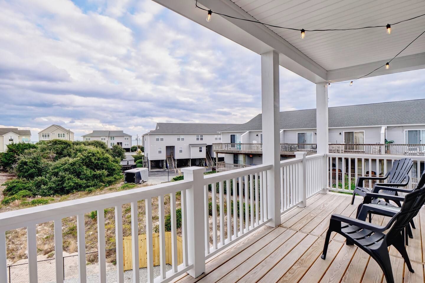 A covered outdoor area with a wooden deck, white railings, and black chairs.