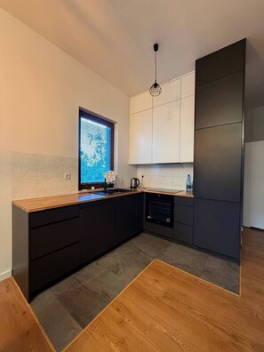 A modern kitchen with dark cabinetry, a wooden countertop, and a built-in oven. - Lumina Premium 2BR Apt w/ Parking I AC (Warszawa)